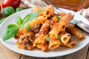 Ziti bolognese on white plate, pasta casserole with minced meat, tomato sauce and cheese, horizontal